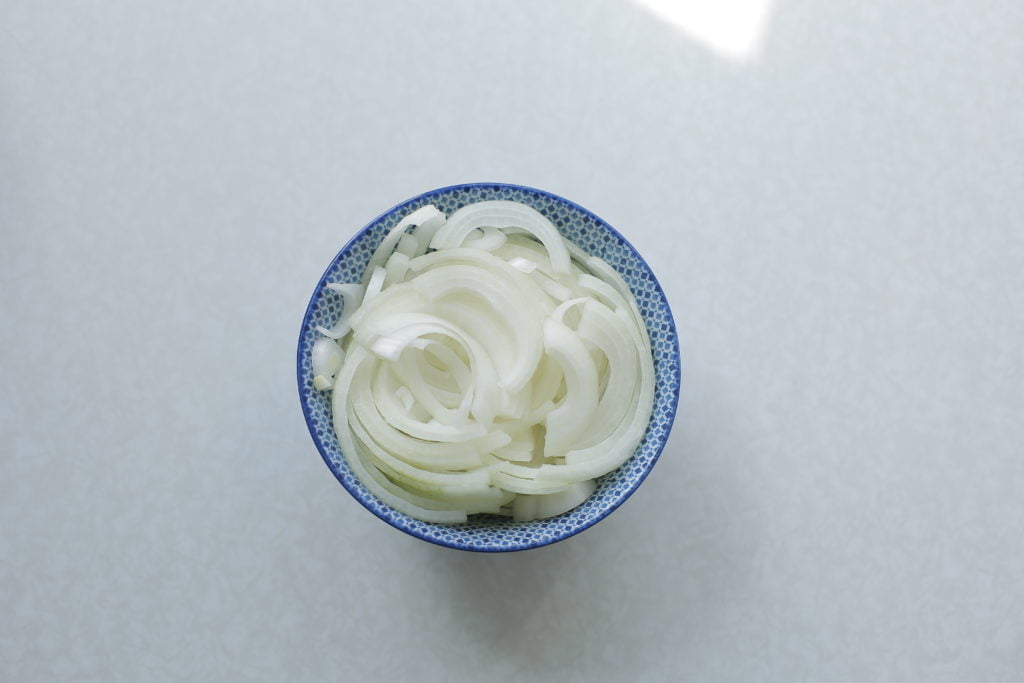 Pel en snijd de gele ui in halve ringen.