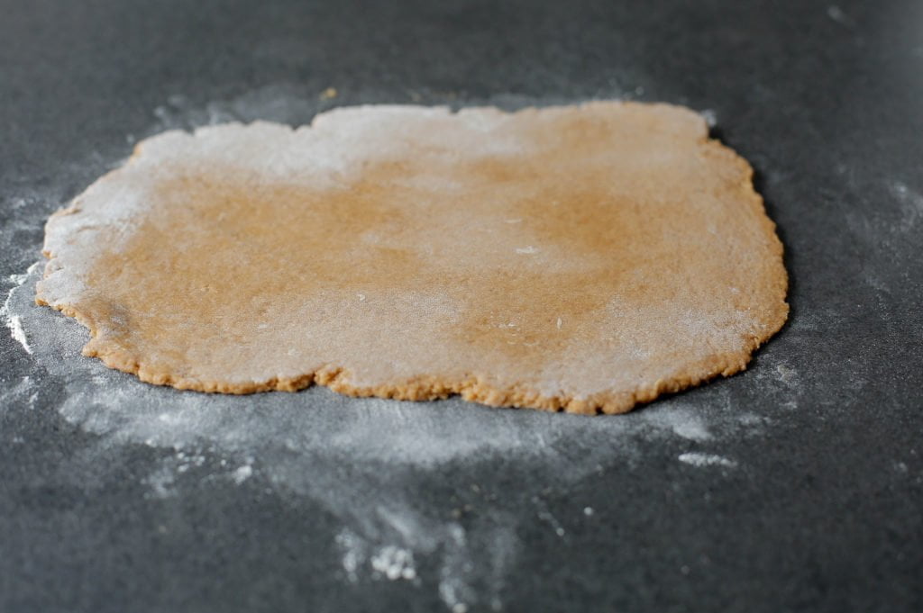 Strooi weer wat bloem op de werkplek en rol het koekjesdeeg (370 gr) uit tot een rechthoekige lap. Leg het koekjesdeeg over de amandelspijs en werk het mooi egaal af.