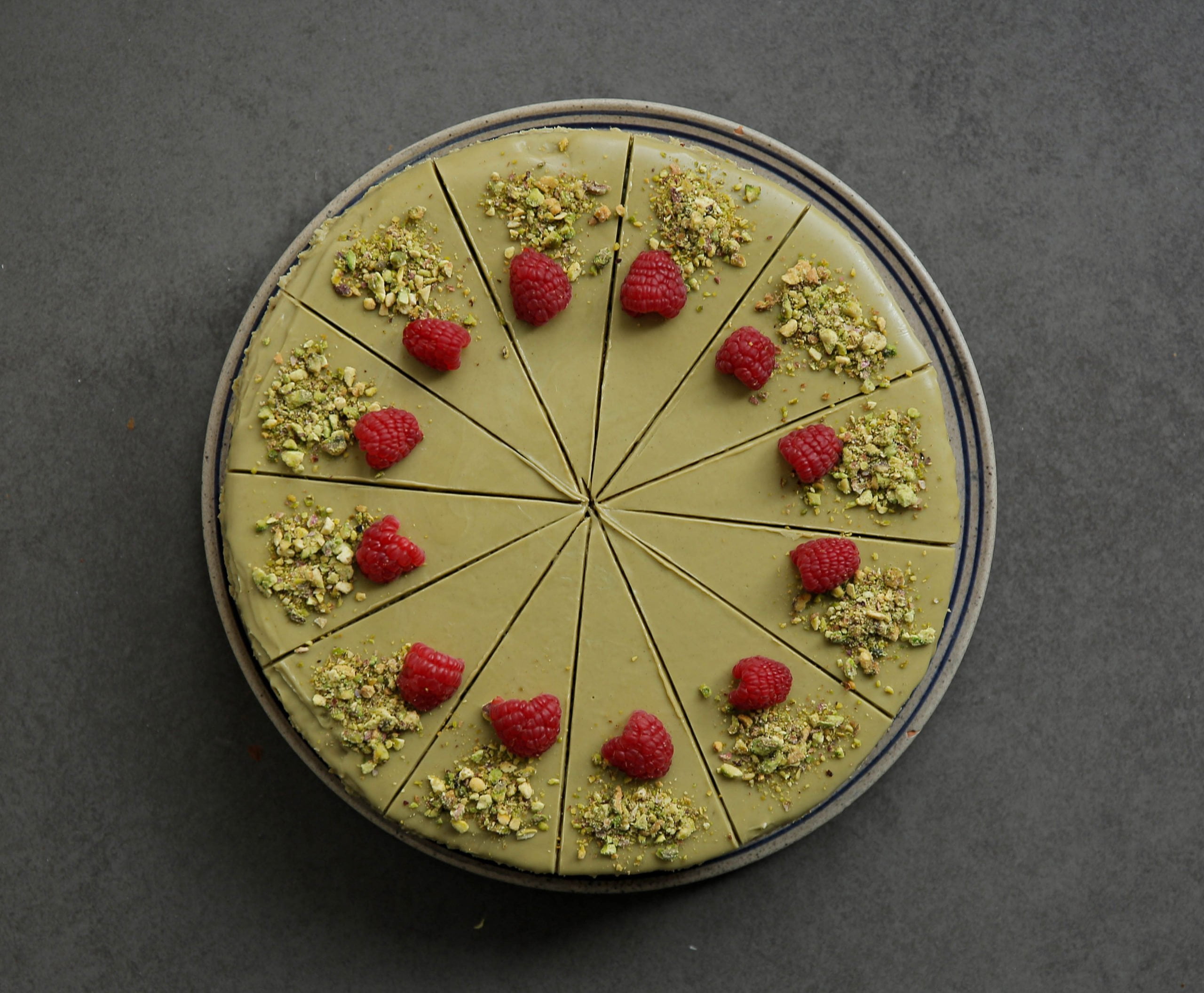 Pistache cheesecake aansnijden en garneren met frambozen en pistachenoten
