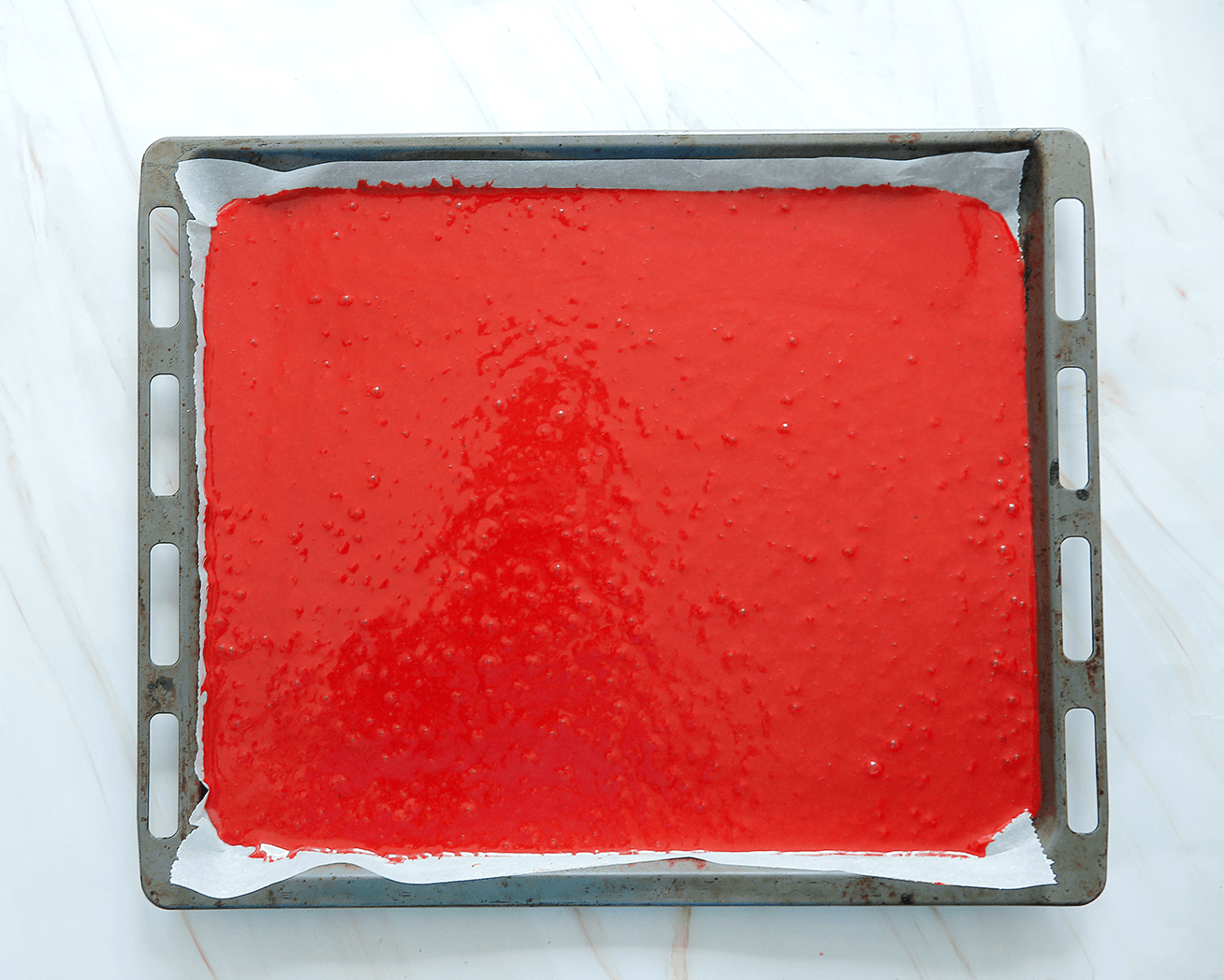 Rode cakebeslag gieten over een bakplaat met bakpapier