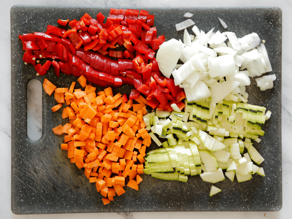 Pel en snipper de gele ui. Snijd de wortel, courgette en rode puntpaprika klein.