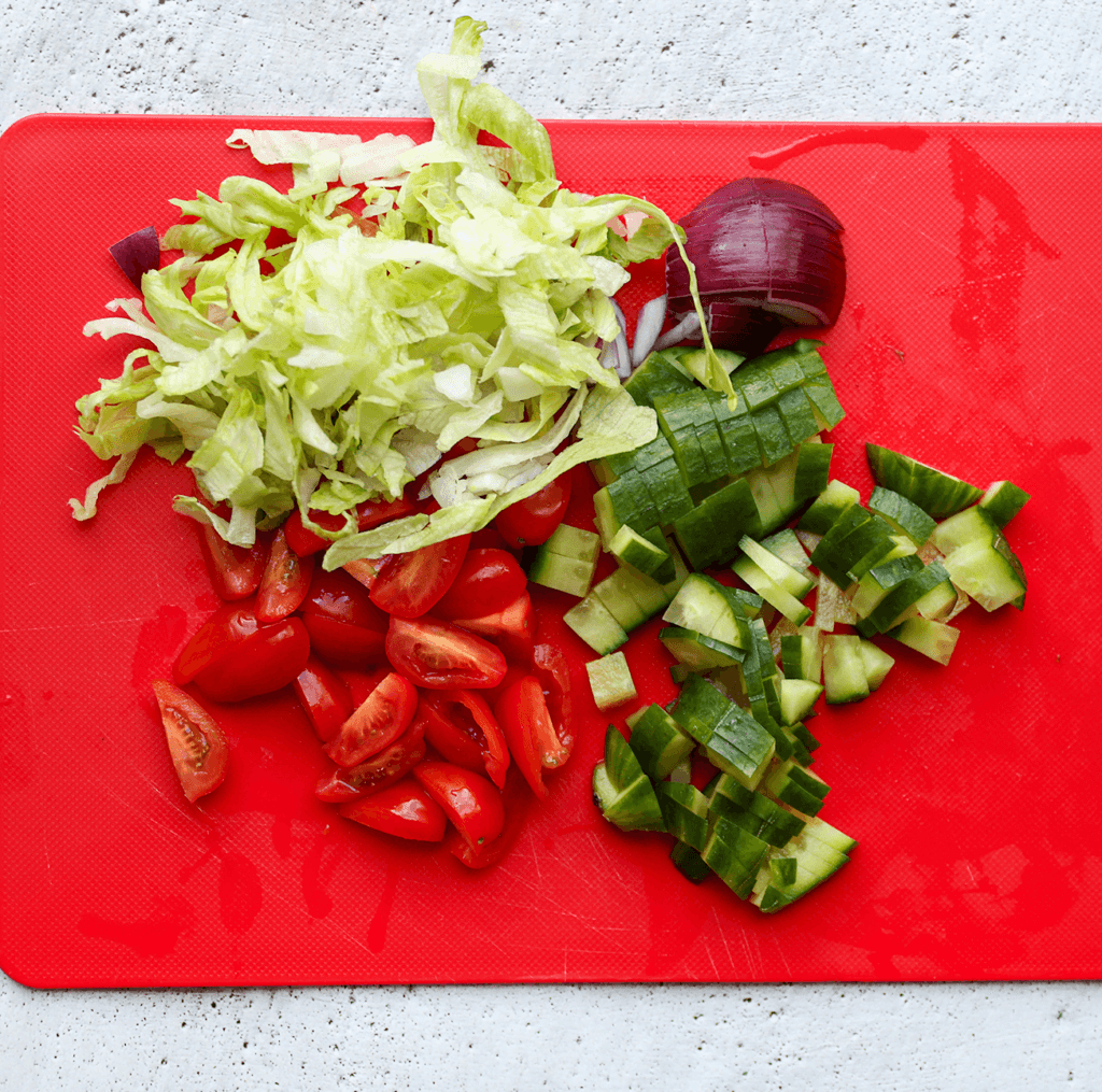 Snijd de ijsbergsla, snoeptomaatjes, rode ui en komkommer in kleine stukken.