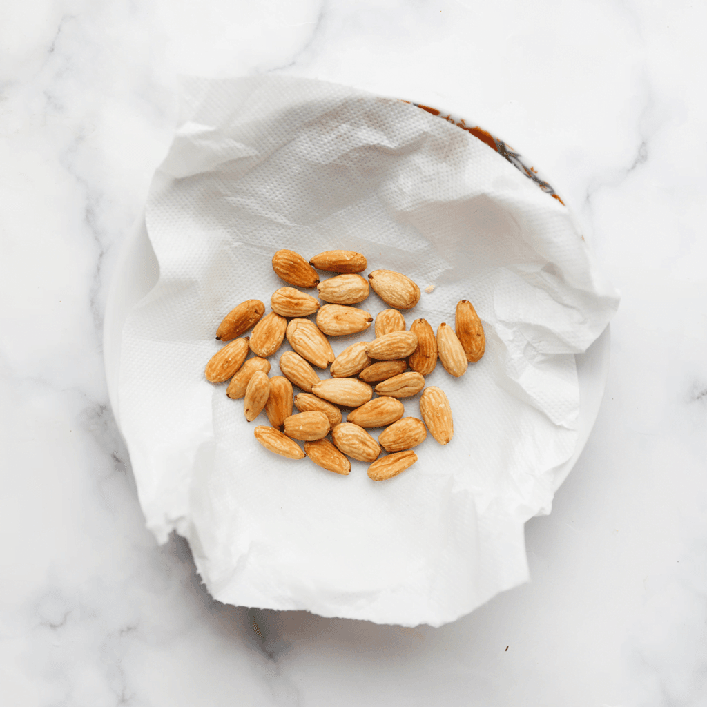 Verhit een laagje zonnebloemolie in een koekenpan op middelhoog vuur. Voeg de gepelde amandelen toe en bak ze tot ze lichtjes goudbruin kleuren. Laat ze er niet te lang in, want ze garen nog verder zodra je ze uit de pan schept. Laat de amandelen uitlekken op een vel keukenpapier.