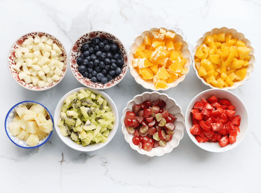 Schil de peer, kiwi en sinaasappel. Snijd de perzik, ananas, kiwi, peer, aardbeien, rode druiven en sinaasappel in stukken.