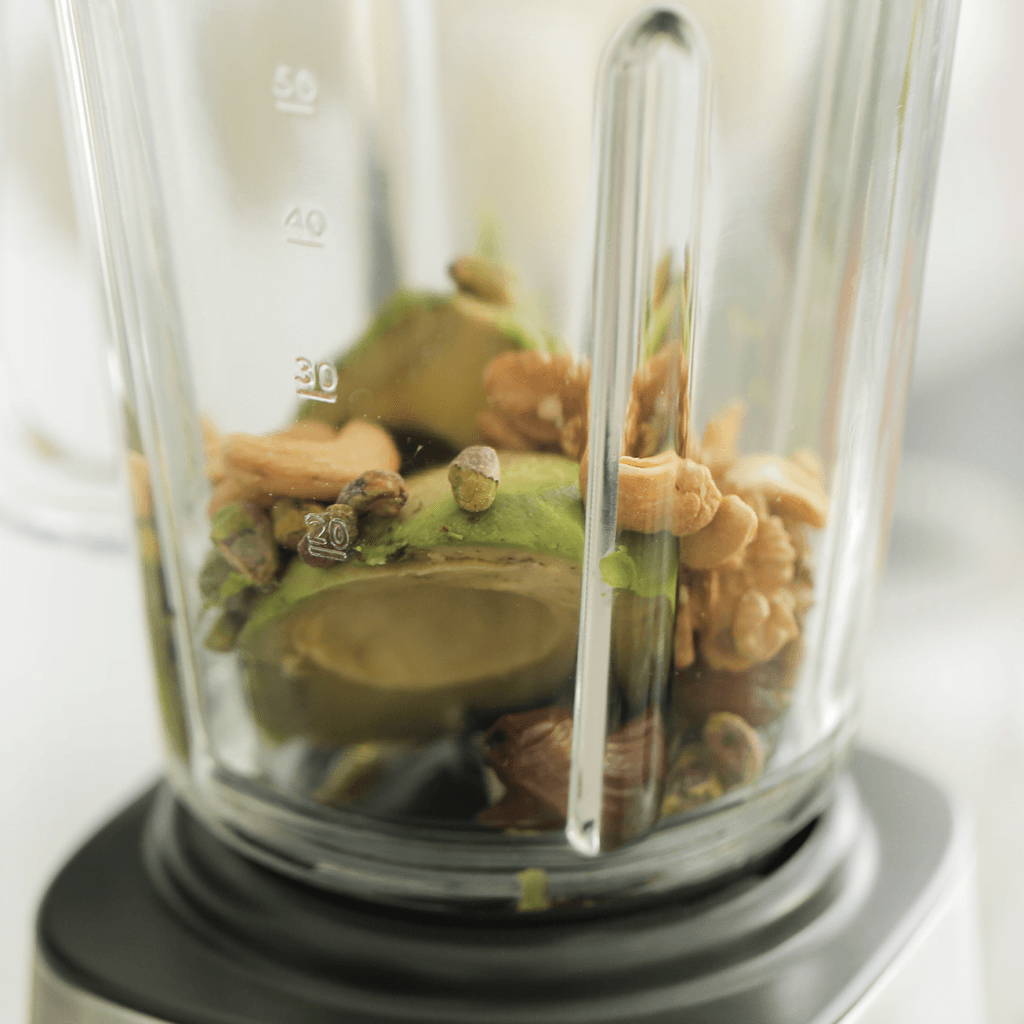 Ontpit de dadels. Snijd de avocado in de lengte doormidden rondom de pit. Draai de avocadohelften in tegengestelde richting om ze van elkaar te scheiden. Verwijder de pit. Neem een lepel en schep het vruchtvlees eruit. Doe dit in een blender. Voeg de dadels, walnoten, pistachenoten, cashewnoten, honing en melk toe. Mix gedurende 2 minuten.