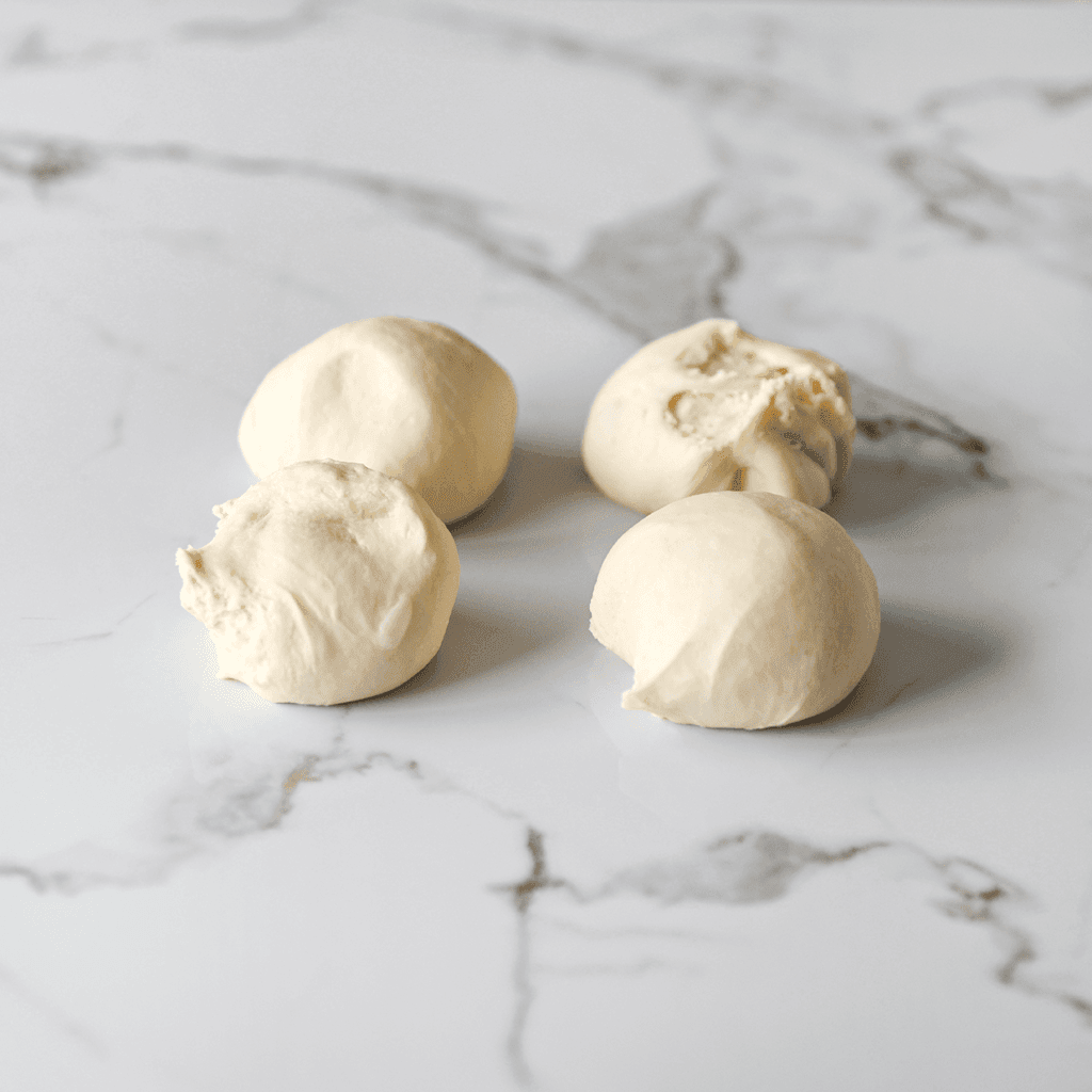 Verdeel het deeg in 4 stukken (100 gram per stuk) en vorm er mooie ronde bolletjes van.