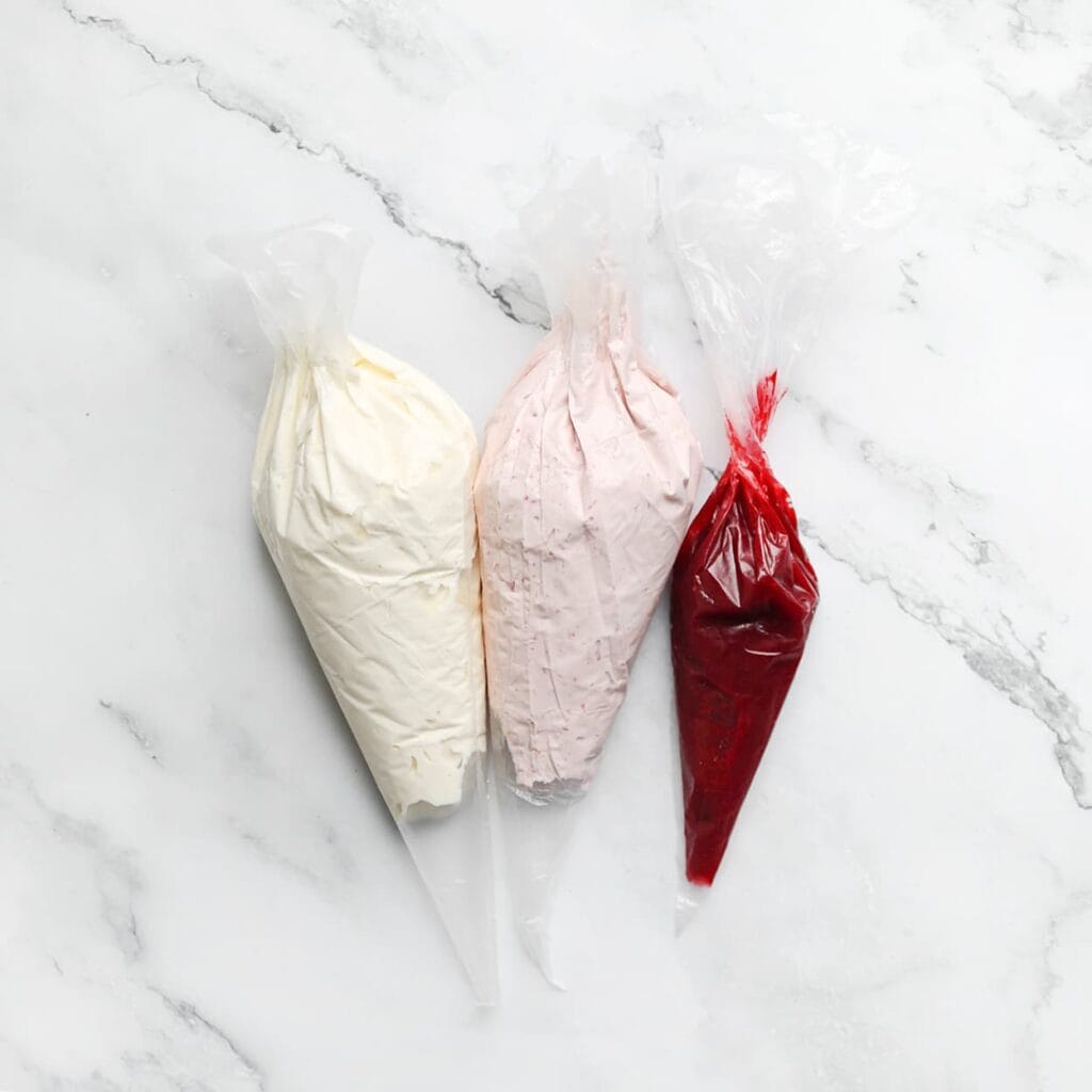 Doe de frambozensiroop, vanilleroom en frambozenroom in een spuitzak.