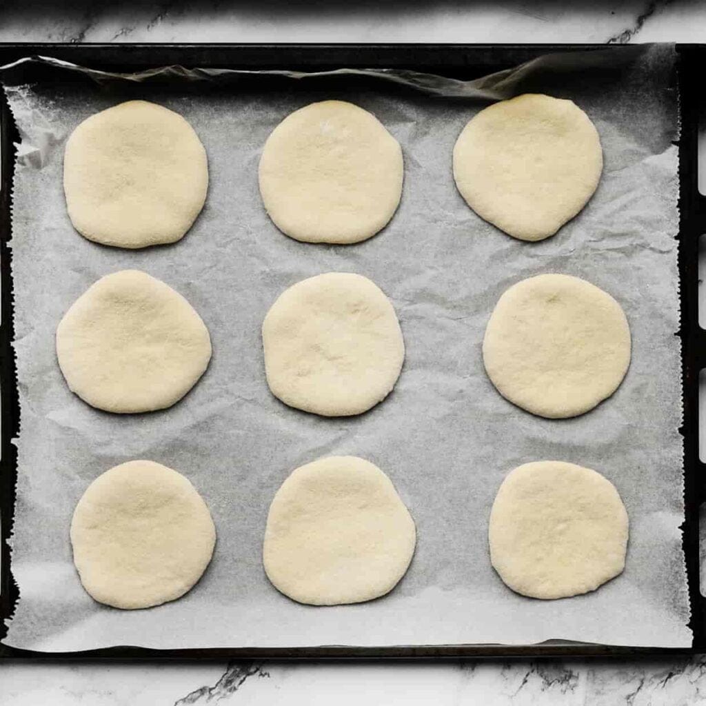 Leg de platte broodjes op een bakplaat bekleed met bakpapier. Laat ze 30 minuten rijzen of tot ze in formaat zijn verdubbeld.