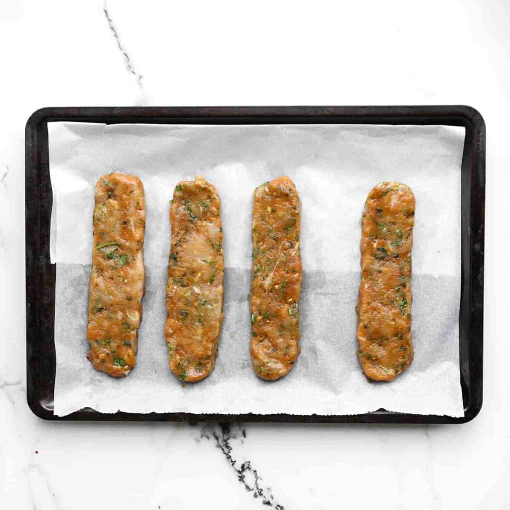 Neem wat van het gehakt en vorm het tot een langwerpige staaf. Leg deze op een bakplaat met bakpapier en druk ze voorzichtig iets plat.