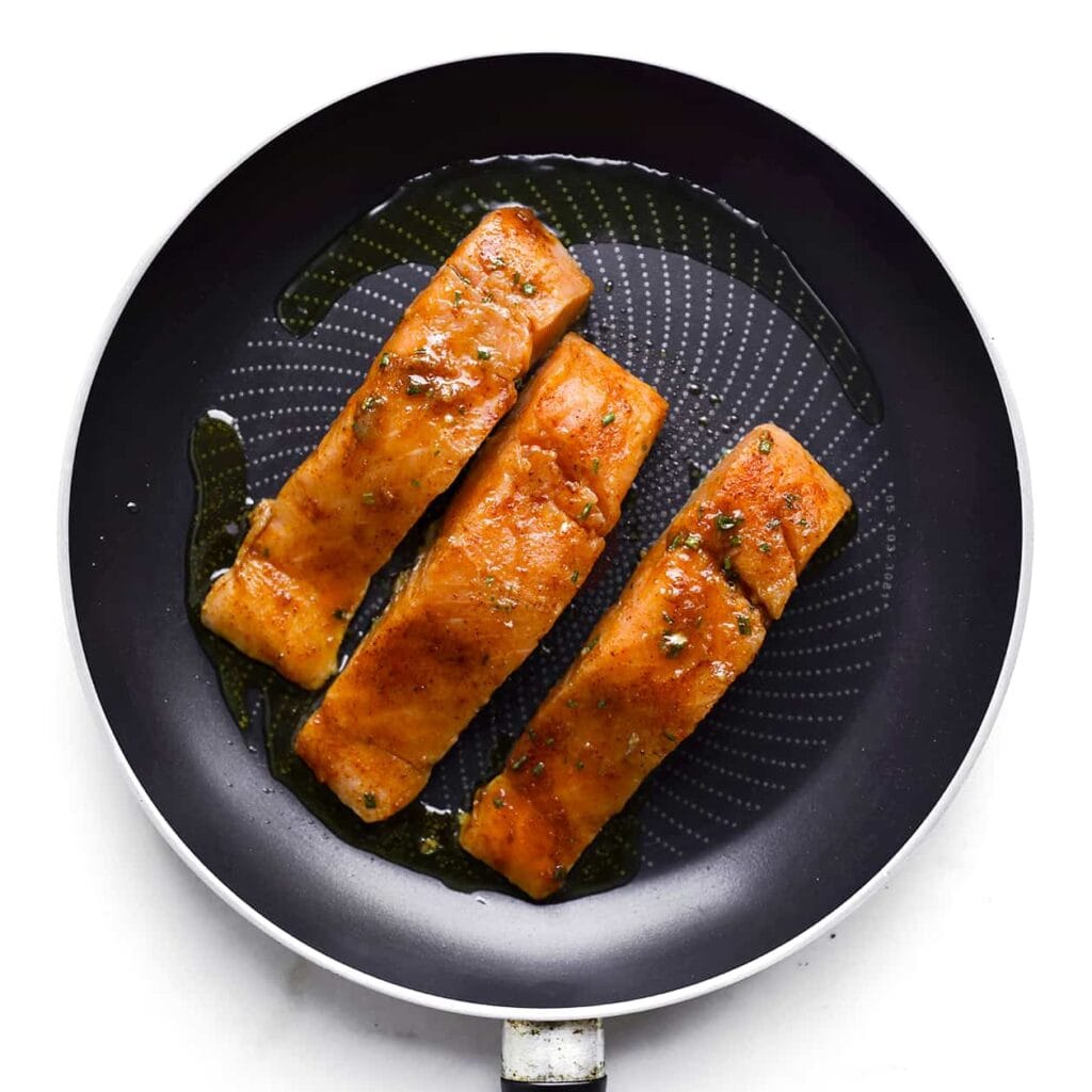 Verhit in een andere koekenpan de roomboter op matig vuur. Bak de zalmfilets 3-4 minuten aan elke kant, tot ze gaar zijn.