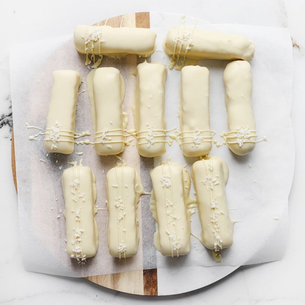 Garneer de kokosbars met dunne lijntjes gesmolten chocolade, geraspte kokos en gevriesdroogde frambozen.