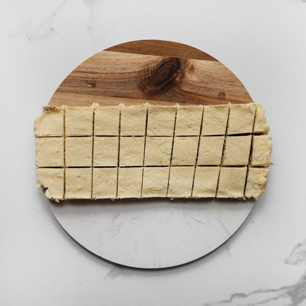 Haal de opgesteven kokoskoek uit de vriezer en snijd deze in gelijke blokjes.