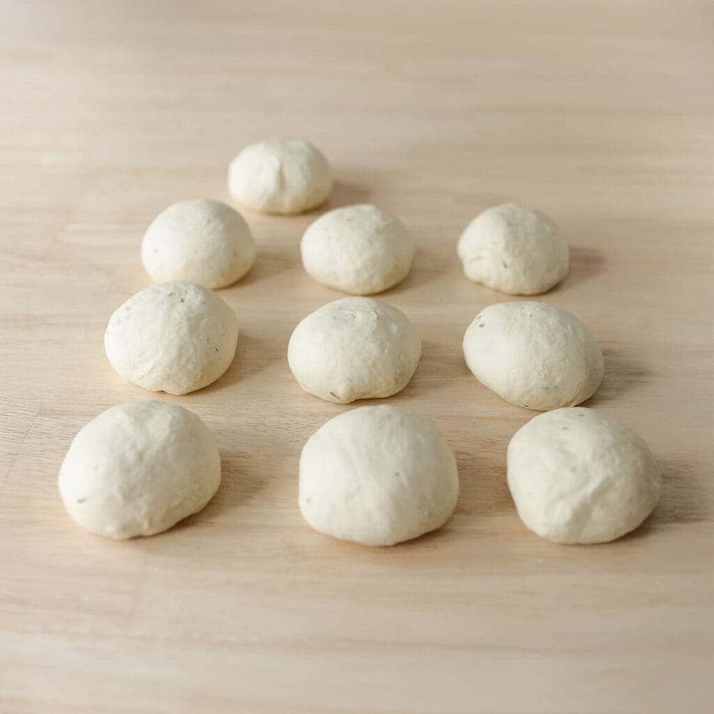 Druk de lucht uit het deeg en verdeel het in 10 gelijke stukken van ongeveer 100 gram. Vorm tot bollen.