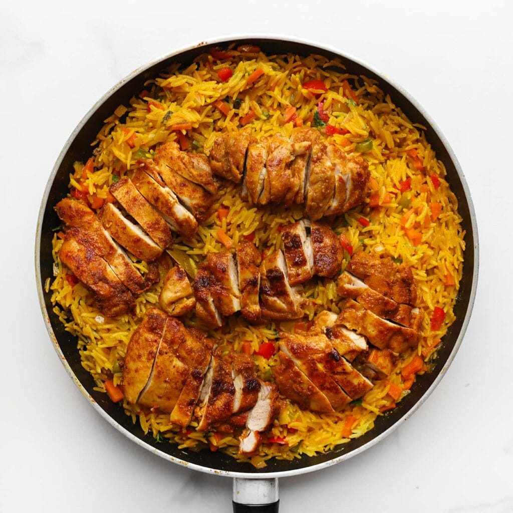 Snijd ondertussen de gebakken kippendijen in reepjes. Zodra de rijst gaar is, leg je de kipreepjes bovenop de rijst. Laat het geheel nog 2 minuten staan met de deksel op de pan, zodat de smaken samenkomen. Serveer warm en garneer eventueel met extra peterselie.