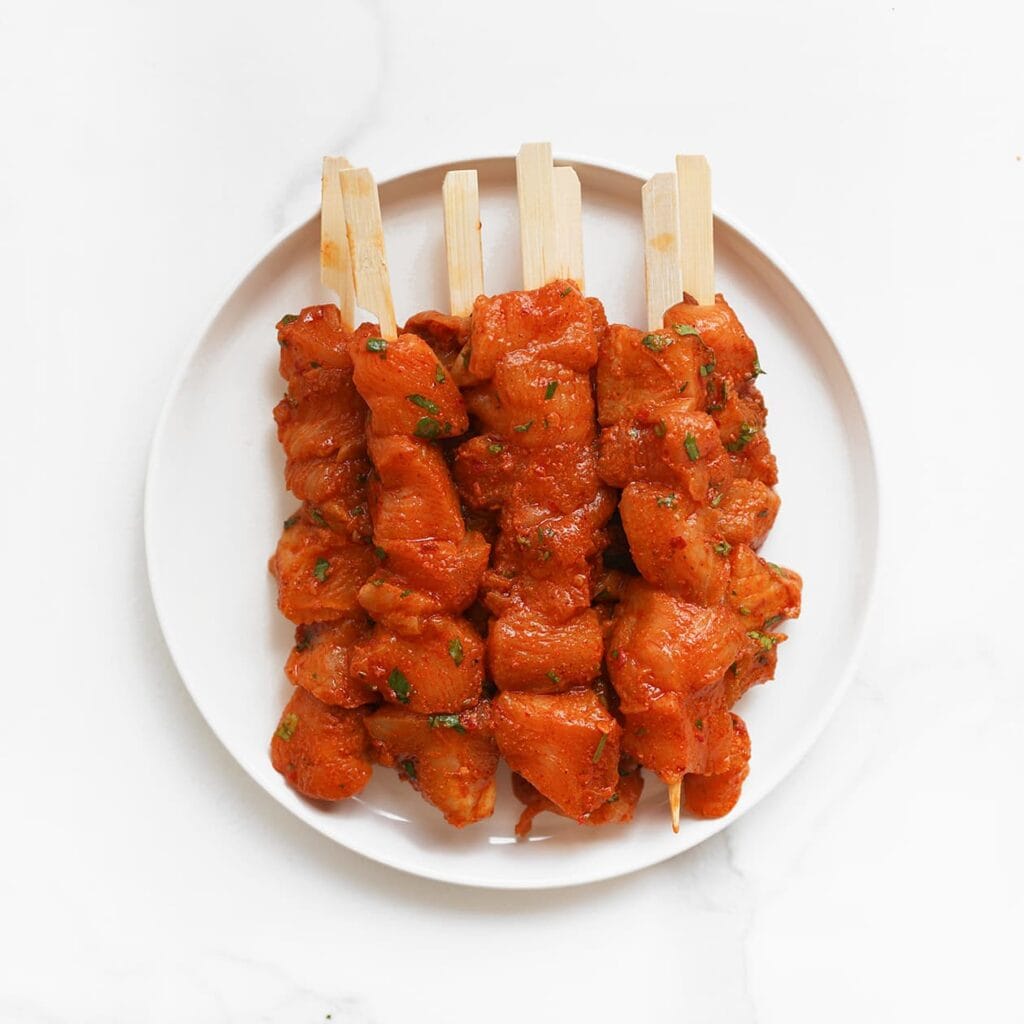 Rijg de gemarineerde kipblokjes aan spiesjes. Zet ze apart.