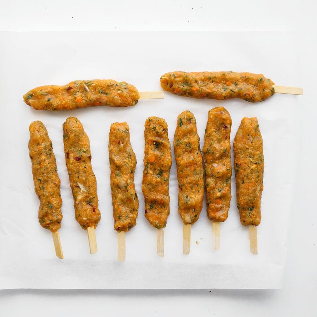 Neem een satéprikker en vorm ongeveer 80 gram van het kipmengsel tot een langwerpige staaf rondom de prikker. Herhaal dit met de rest van het mengsel.