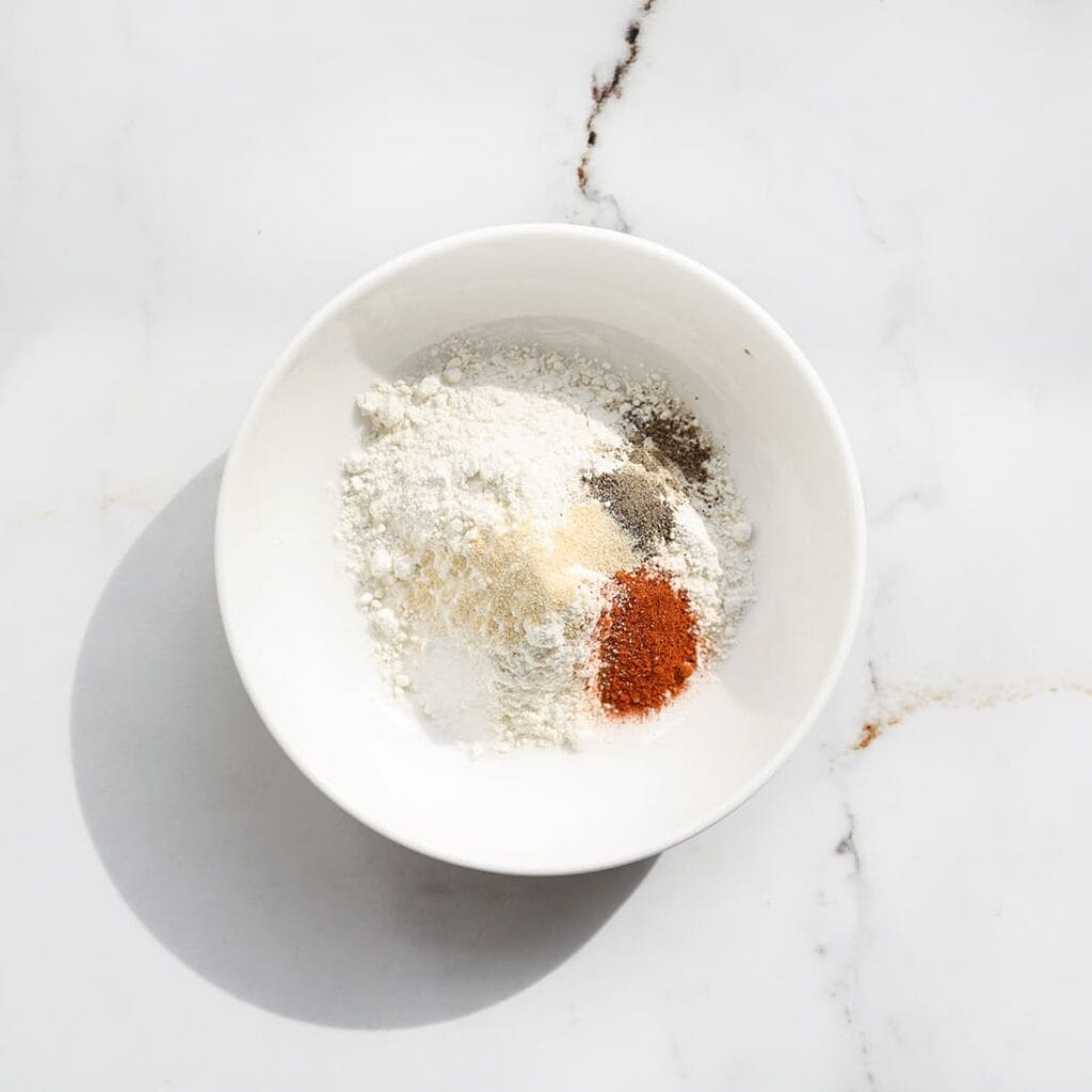 Meng in een andere kom de bloem, het zout, de zwarte peper en uienpoeder.