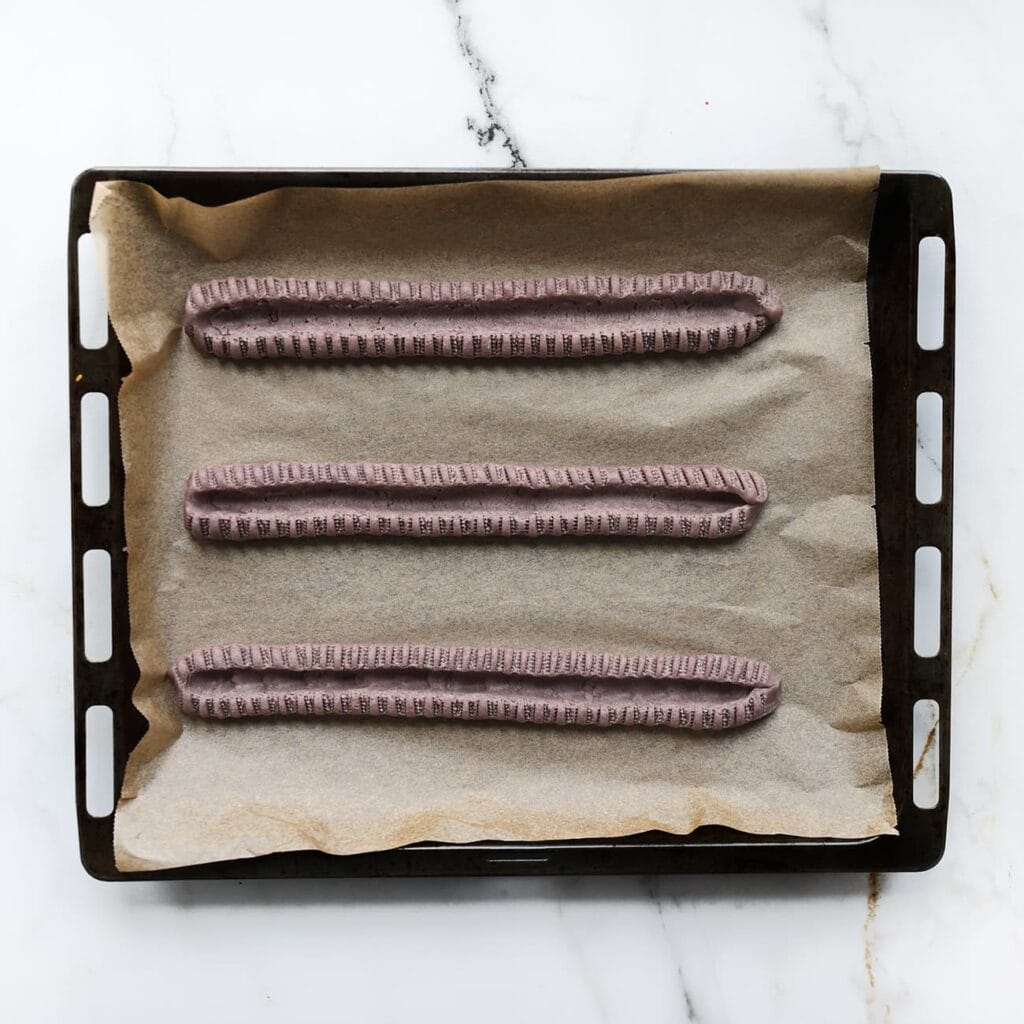 Leg de strengen op een bakplaat met bakpapier. Maak opnieuw een verdieping in het midden en knijp met het tangetje langs de randen.
