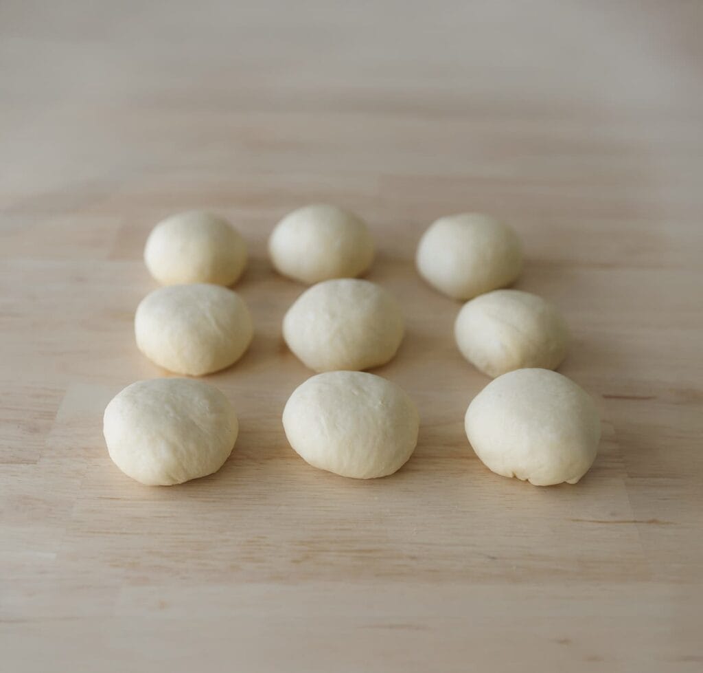 Druk de lucht uit het deeg en verdeel het in 8 gelijke stukken van ongeveer 85 gram. Vorm tot bollen.