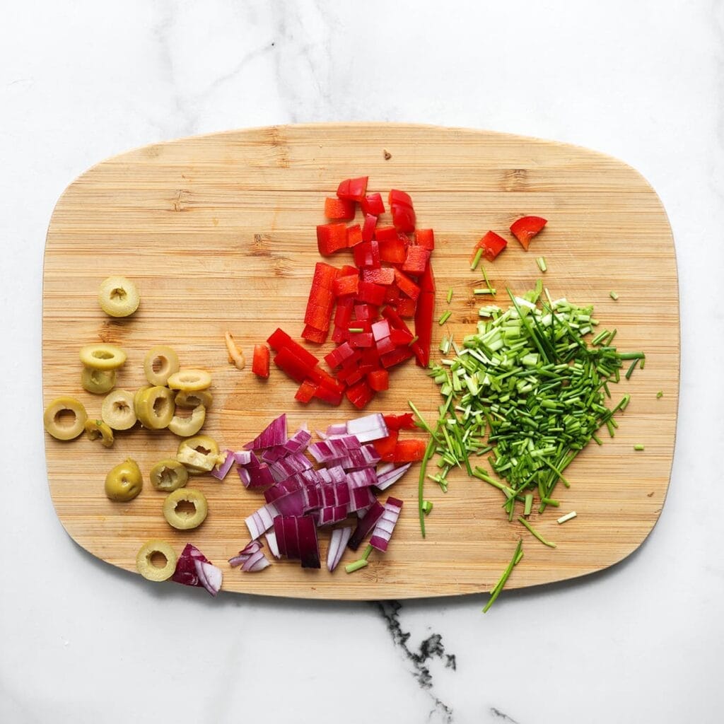 Snijd de rode paprika in kleine blokjes, de groene olijven in plakjes en de rode ui in stukken. Hak de bieslook.