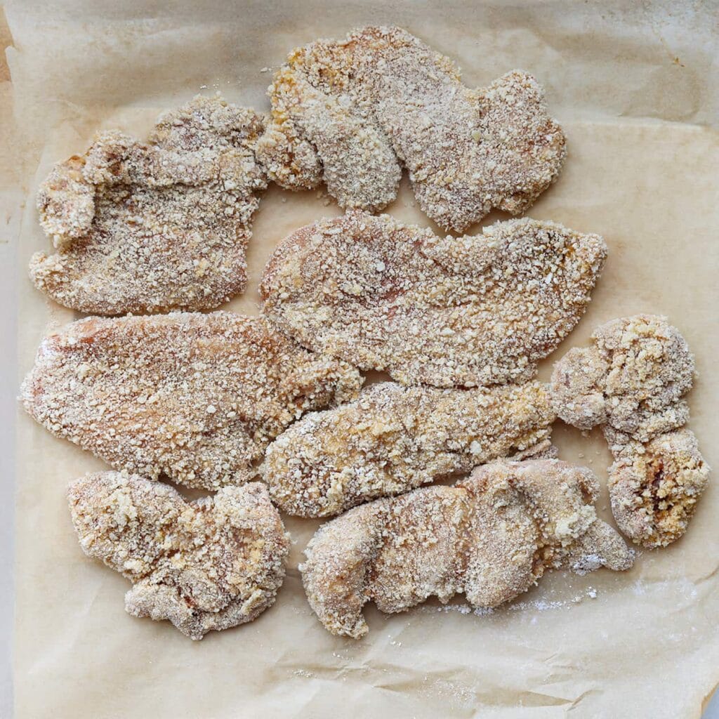 Leg de kip op een vel bakpapier. Je kunt de gepaneerde kip eventueel kort in de vriezer leggen om de coating beter te laten hechten.