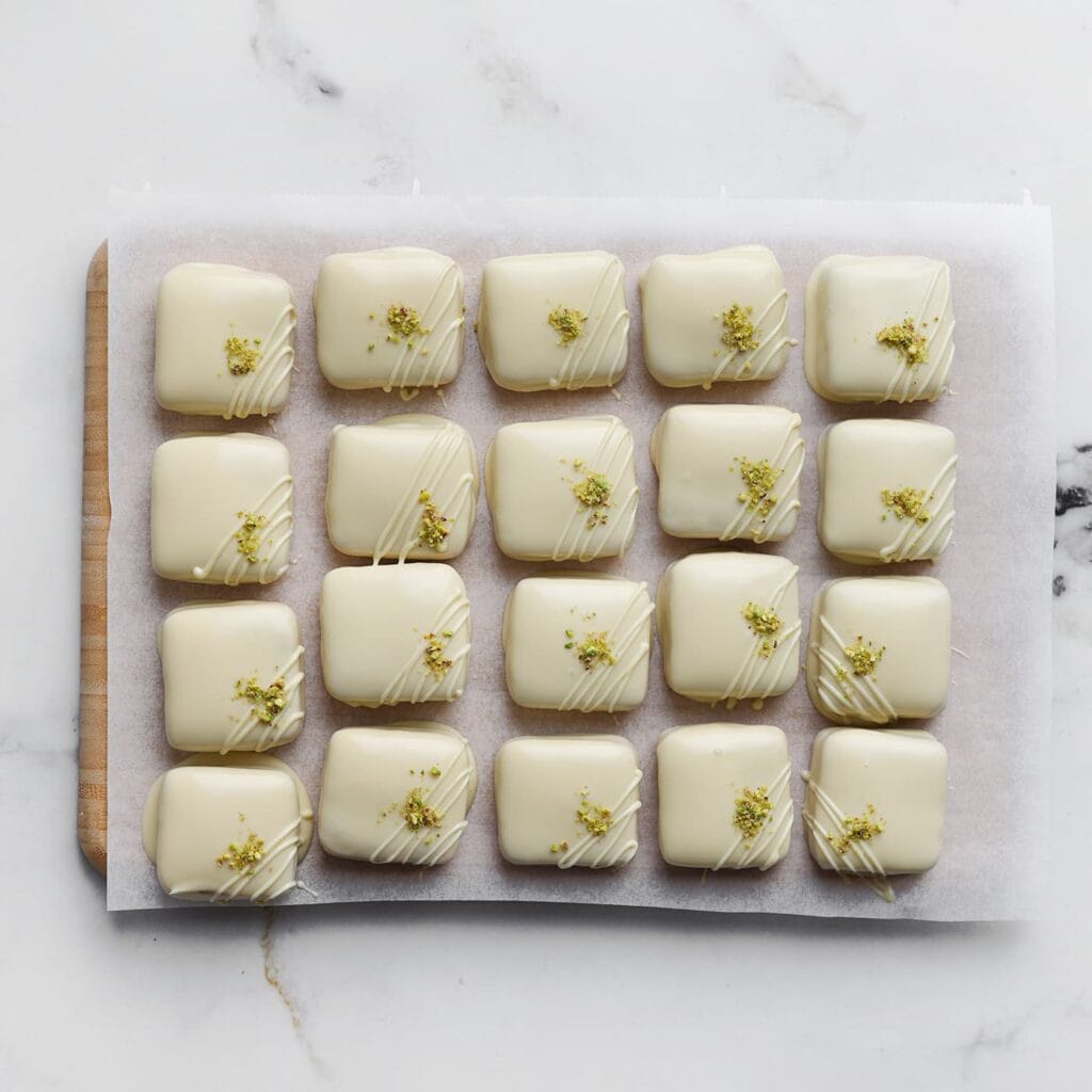 Decoreer met dunne lijntjes witte chocolade, gehakte pistachenoten en eetbare rozenblaadjes. Laat de chocolade volledig uitharden.