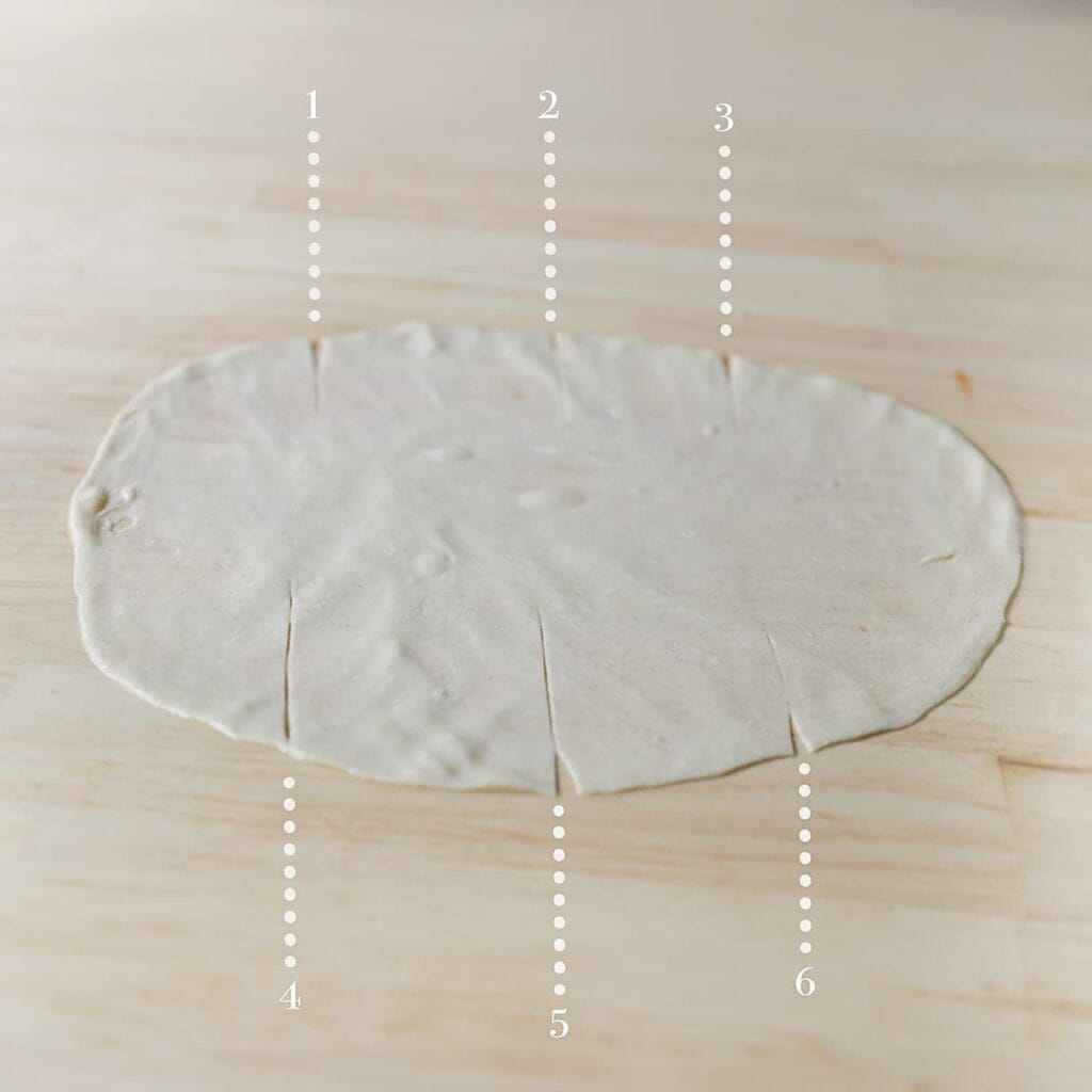 Snijd met een pizzasnijder 6 inkepingen aan de randen zodat vouwen makkelijker gaat. Vouw het deeg per deel tot een mooi pakketje.