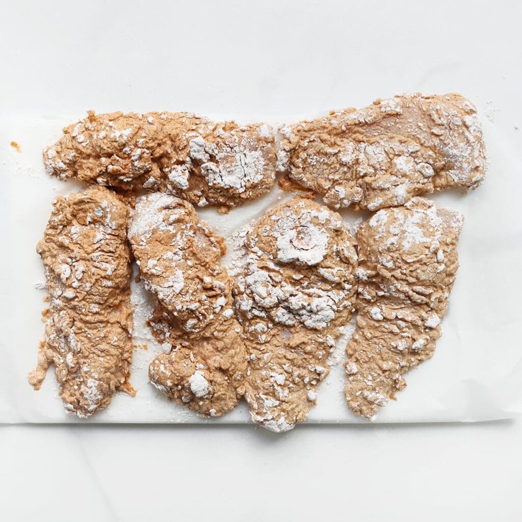 Leg de gepaneerde kip op een vel bakpapier.